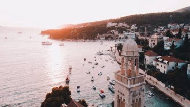 Aerial view of the historic bell tower in Hvar, Croatia, overlooking a harbor filled with boats during sunset.