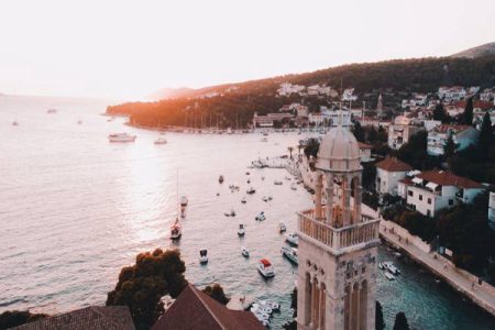 Aerial view of the historic bell tower in Hvar, Croatia, overlooking a harbor filled with boats during sunset.